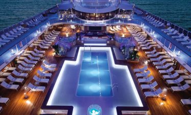 A cruise ship pool deck at night, lined with lounge chairs