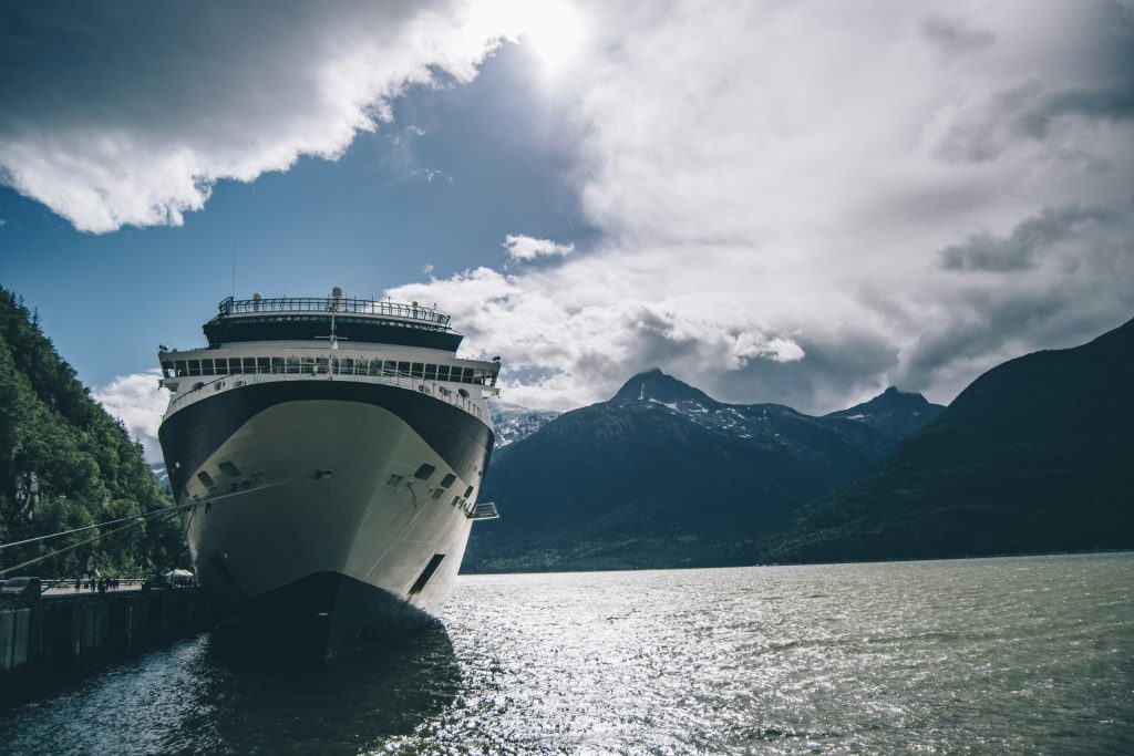 Bow of a cruise ship docked beside forested mountains under dramatic clouds in Southeast Alaska
